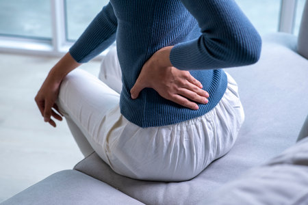 Woman suffering from back ache on the sofa. Female with back pain at homeの写真素材