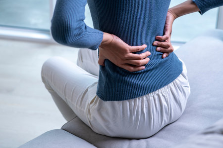 Woman suffering from back ache on the sofa. Female with back pain at home.の写真素材