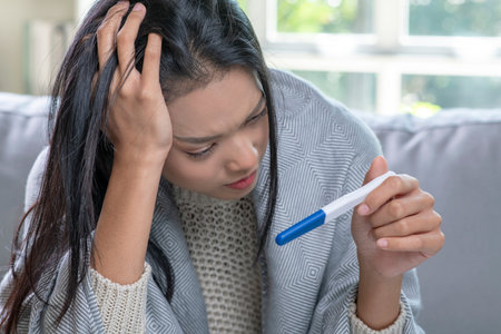 Depressed young Asian woman holding negative or positive pregnancy test.の写真素材