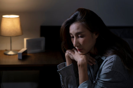 Young Asian woman in bedroom feeling sad tired and worried suffering depression in mental health, woman sitting in bed cannot sleep from insomnia.の写真素材