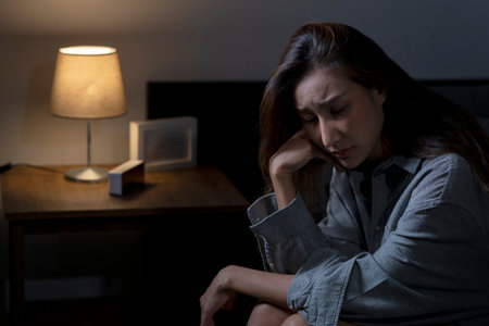 Young Asian woman in bedroom feeling sad tired and worried suffering depression in mental health, woman sitting in bed cannot sleep from insomnia.の写真素材