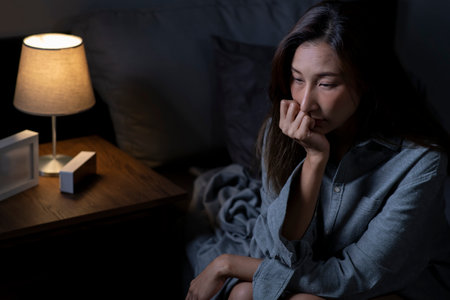 Young Asian woman in bedroom feeling sad tired and worried suffering depression in mental health, woman sitting in bed cannot sleep from insomnia.の写真素材