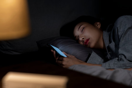 Young Asian woman using smartphone in bed cannot sleep from insomnia, depressed woman in bedroomの写真素材