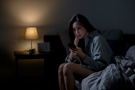 Young Asian woman using smartphone in bed cannot sleep from insomnia, depressed woman in bedroomの写真素材