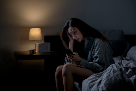 Young Asian woman using smartphone in bed cannot sleep from insomnia, depressed woman in bedroomの写真素材