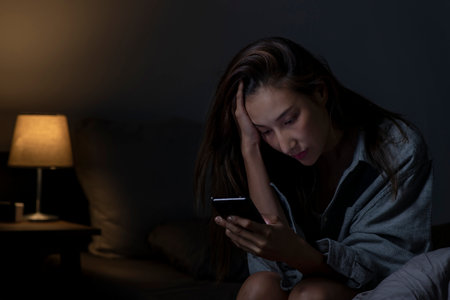 Young Asian woman using smartphone in bed cannot sleep from insomnia, depressed woman in bedroomの写真素材