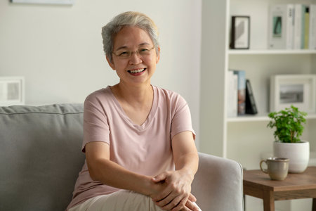 Portrait of smiling Asian senior woman sitting on sofa at homeの写真素材