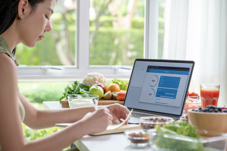 Asian woman professional nutritionist working and checking data from a laptop with a variety of fruits, nuts, vegetables, and dietary supplements on the tableの写真素材