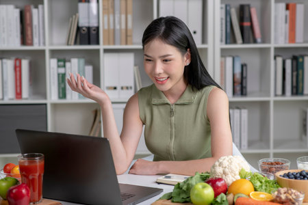 Asian woman professional nutritionist consulting with her client on laptop, surrounded by a variety of fruits, nuts, vegetables, and dietary supplements on the tableの写真素材