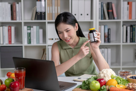Asian woman professional nutritionist consulting with her client on laptop, surrounded by a variety of fruits, nuts, vegetables, and dietary supplements on the tableの写真素材