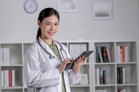 Portrait of beautiful Asian woman doctor holding digital tablet and looking at camera. Confident female doctor using digital tablet in medical office.の写真素材