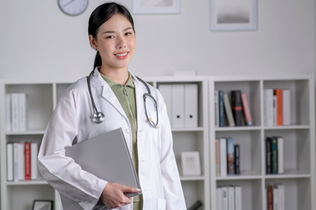 Portrait of beautiful smiling female Asian doctor standing in medical office. Health care concept, medical insurance, copy space.の写真素材