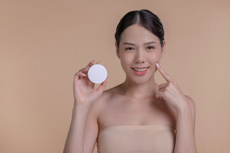 Portrait of a young Asian woman smiling holding mockup product for advertising text place, beige background. Concept of healthcare for skin, beauty care product for advertising.の写真素材