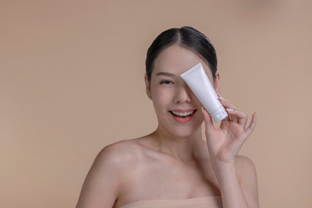 Portrait of a young Asian woman smiling holding mockup product for advertising text place, beige background. Concept of healthcare for skin, beauty care product for advertising.の写真素材