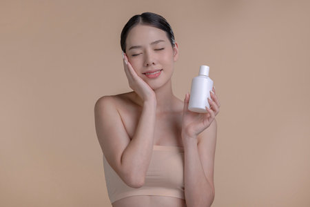 Portrait of a young Asian woman smiling holding mockup product for advertising text place, beige background. Concept of healthcare for skin, beauty care product for advertising.の写真素材
