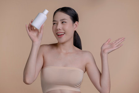 Portrait of a young Asian woman smiling holding mockup product for advertising text place, beige background. Concept of healthcare for skin, beauty care product for advertising.の写真素材
