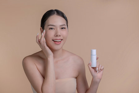 Portrait of a young Asian woman smiling holding mockup product for advertising text place, beige background. Concept of healthcare for skin, beauty care product for advertising.の写真素材