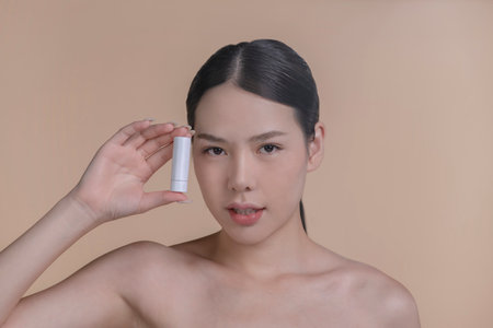 Portrait of a young Asian woman smiling holding mockup product for advertising text place, beige background. Concept of healthcare for skin, beauty care product for advertising.の写真素材