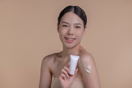 Portrait of a young Asian woman smiling holding mockup product for advertising text place, beige background. Concept of healthcare for skin, beauty care product for advertising.の写真素材