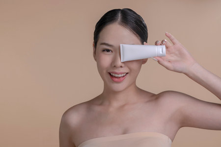 Portrait of a young Asian woman smiling holding mockup product for advertising text place, beige background. Concept of healthcare for skin, beauty care product for advertising.の写真素材