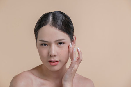Beautiful Asian woman applying hyaluronic serum on her face. Photo of attractive woman with perfect makeup on beige background. Beauty conceptの写真素材
