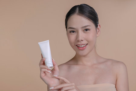 Portrait of a young Asian woman smiling holding mockup product for advertising text place, beige background. Concept of healthcare for skin, beauty care product for advertising.の写真素材