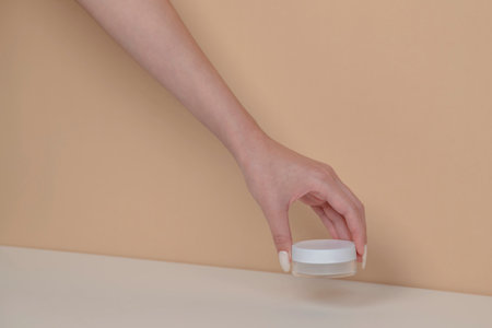 Woman hand is picking up the blank cosmetic packaging mockup: white bottle on beige background.の写真素材