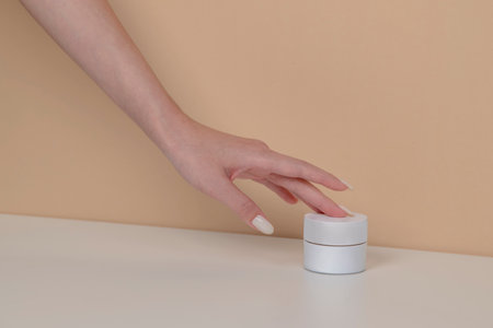 Woman hand is picking up the blank cosmetic packaging mockup: white bottle on beige background.の写真素材