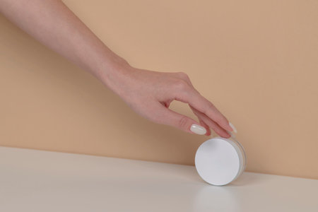 Woman hand is picking up the blank cosmetic packaging mockup: white bottle on beige background.の写真素材