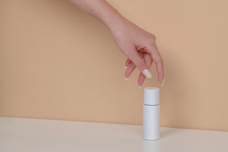 Woman hand is picking up the blank cosmetic packaging mockup: white bottle on beige background.の写真素材