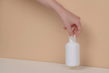 Woman hand is picking up the blank cosmetic packaging mockup: white bottle on beige background.の写真素材