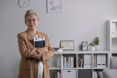 Image of professional Asian female psychologist standing, looking and smiling at camera, working in modern office. Psychotherapy services, mental health professional conceptの写真素材