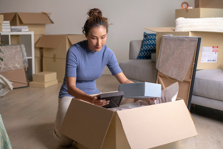 Young Asian woman moving into new house holding and unpacking her belongings with cardboard boxes.の写真素材