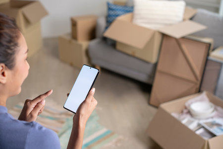 Young Asian woman sitting in new house using smartphone buying decorations online after moving in.の写真素材