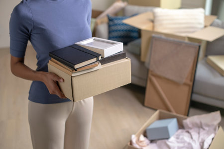Young woman moving into new apartment holding and unpacking her belongings with cardboard boxes.の写真素材