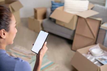 Young Asian woman sitting in new house using smartphone buying decorations online after moving in.の写真素材