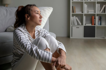 Young Asian woman sitting on floor at home feeling sad tired and worried suffering depression in mental health.Female suffer from mental health problems.の写真素材