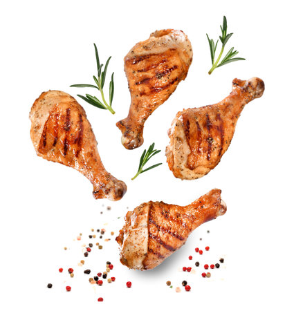 Grilled chicken legs or drumsticks falling down with herbs and colourful peppers isolated on white background. Juicy BBQ chicken drumsticks sprinkled with herbs and seasoning on white background.の写真素材
