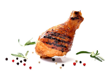 Juicy and delicious grilled chicken leg or drumstick on white surface with herbs, rosemary and colourful peppers and seasoning isolated on white background.の写真素材