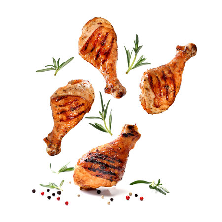 Grilled chicken legs or drumsticks falling down with herbs and colourful peppers isolated on white background. Juicy BBQ chicken drumsticks sprinkled with herbs and seasoning on white background.の写真素材