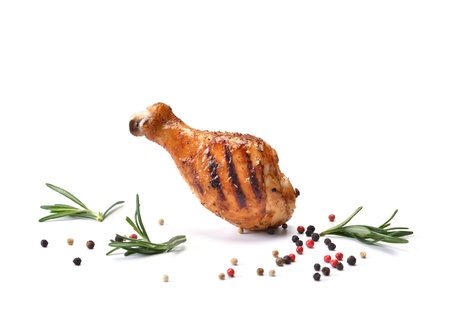 Juicy and delicious grilled chicken leg or drumstick on white surface with herbs, rosemary and colourful peppers and seasoning isolated on white background.の写真素材