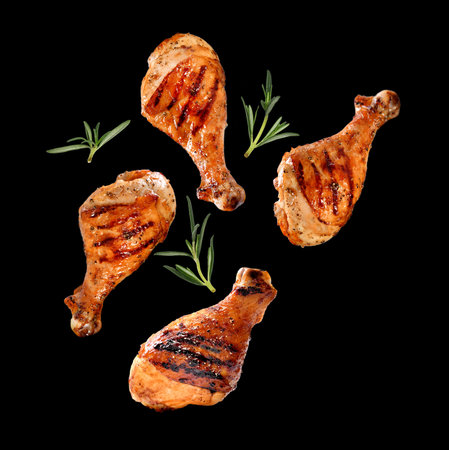 Grilled chicken legs or drumsticks falling down with herbs and colourful peppers isolated on black background. Juicy BBQ chicken drumsticks sprinkled with herbs and seasoning on black background.の写真素材