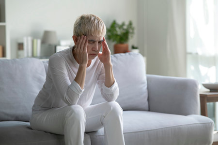 Elderly woman suffering from fever, headache and migraine sitting on sofa at home.の写真素材