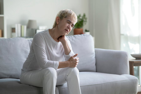 Asian senior woman suffering from neck and shoulder pain on sofa at homeの写真素材