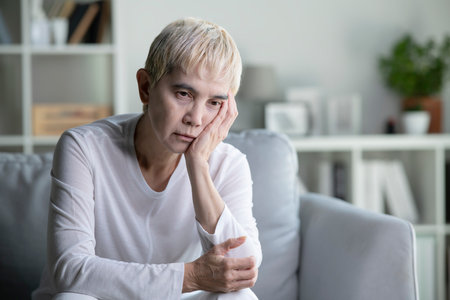 An elderly Asian woman is mentally ill, sad and unhappy. Asian woman, depressed, lonely and anxious, sits on a sofa at home.の写真素材