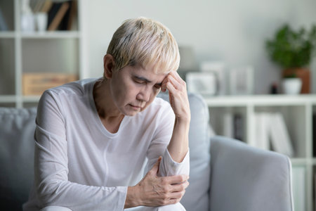 Unhappy Asian senior woman suffering from mental illness and headache. Elderly woman sits alone suffering from physical and mental illness at home.の写真素材