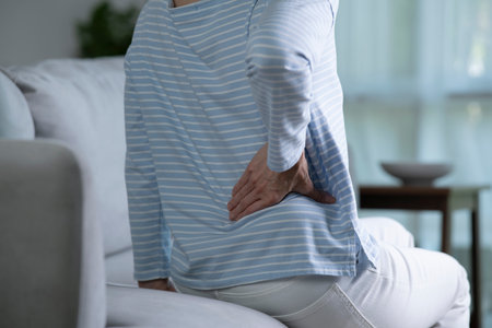 Asian senior woman on sofa feeling and suffering from back pain and lower lumbar discomfort and muscle pain wake up with backache after uncomfortable sleep concept, close up rear viewの写真素材
