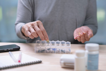 A middle-aged woman holds pills, taken from a daily pill box.の写真素材
