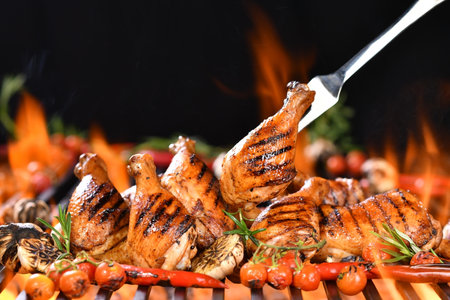 Grilled chicken legs, drumsticks and thighs on the hot flaming barbecue grill with smoke on dark background.の写真素材