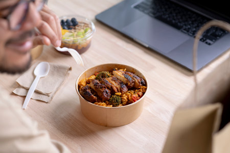 Young Asian man eating healthy meal while working, Businessman having a lunch break at the office, focus on foodの写真素材